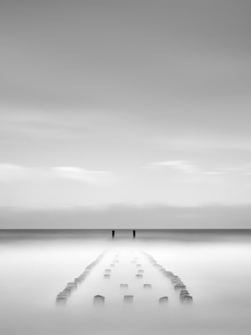 Wooden breakwater poles near Westkapelle gradually disappearing in the North Sea, in black & white. Vanishing - Copyright 2024 Johan Peijnenburg - NiO Photography