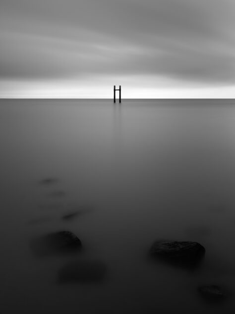 A mooring post at the North Sea coast near Westkapelle in the Netherlands, captured in black & white on a moody day. The Mooring Post - Copyright 2024 Johan Peijnenburg - NiO Photography