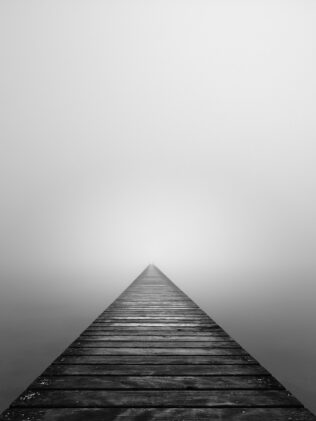 An old wooden pier disappearing into the mist above Lac de Neuchâtel in Switzerland, in black & white. The Abyss - Copyright 2022 Johan Peijnenburg - NiO Photography