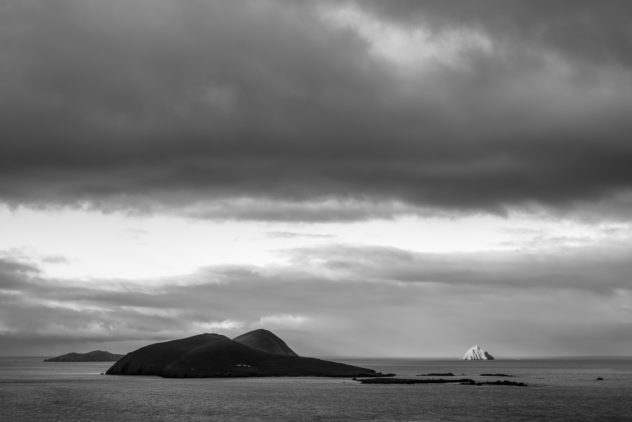 A coastal landscape in B&W with first morning light warming Tearaght Island during a moody sunrise at the Blasket Islands near the Dingle Peninsula in Ireland. Awakening - Copyright Johan Peijnenburg - NiO Photography