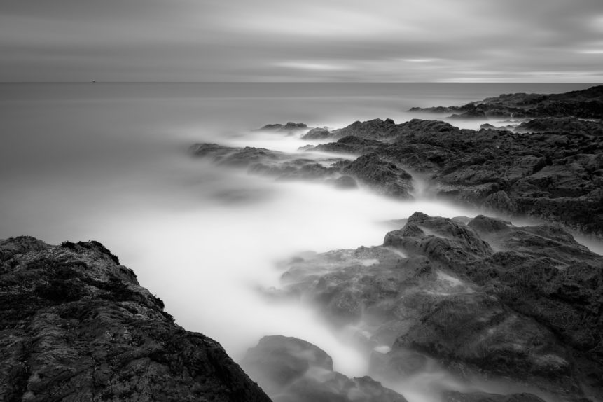 The Irish Sea coast in B&W, with a passing freight ship and the rugged shores near Greystones Beach in Wicklow, Ireland. An Irish Point of View - Copyright Johan Peijnenburg - NiO Photography