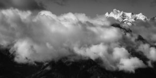 A black and white landscape showing the Swiss mountain peaks Dom, Nadelhorn and Täschhorn, lit by early morning light above a layer of clouds and fog. High above the Clouds - Copyright Johan Peijnenburg - NiO Photography