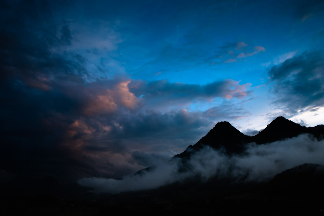 A landscape in colour, featuring two mountains peaks at sunset against a vibrant blue sky as well as clouds and fog. Colourful alpine sunset - Copyright Johan Peijnenburg - NiO Photography