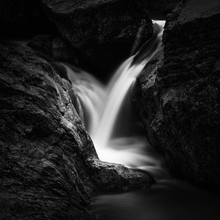 A silky smooth waterfall in a dark cave, with water from a mountain creek dancing around the granite rocks, in black & white. Dancing in the Dark - Copyright Johan Peijnenburg - NiO Photography