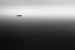 A fisherman at work on his boat on a misty Lac Léman (Lake Geneva) in Switzerland with the French Alps in the background. A Day at the Office - Copyright Johan Peijnenburg - NiO Photography