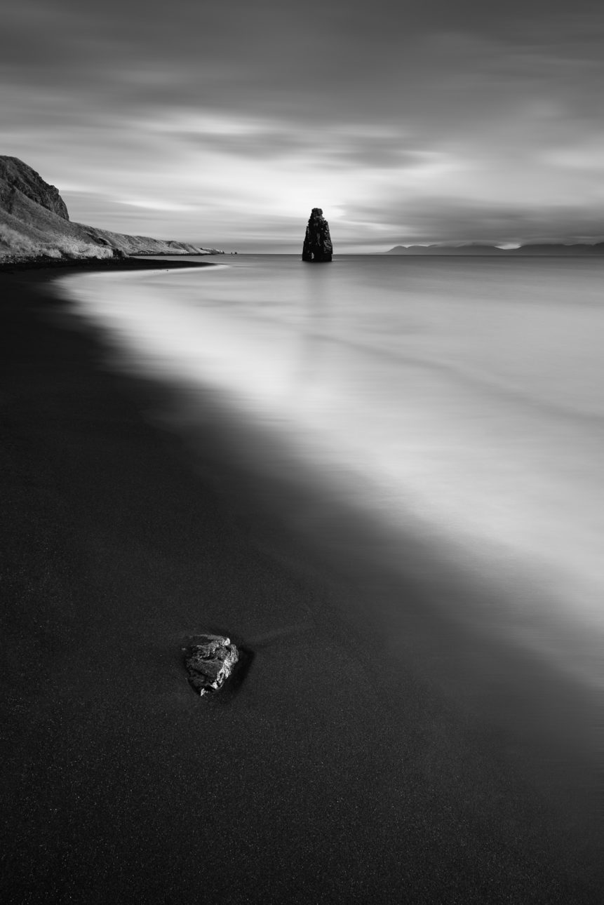 A black sand beach with a rock and Hvítserkur, a basalt sea stack at the eastern shore of the Vatnsnes peninsula in northwest Iceland, in a coastal landscape in B&W. The Troll - Copyright Johan Peijnenburg - NiO Photography