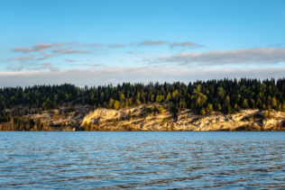 Lac de Joux near L'Abbaye in Switzerland, with soft sunrise light on the trees and rocky shores of the lake. In the Light - Copyright Johan Peijnenburg - NiO Photography