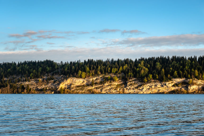 Lac de Joux near L'Abbaye in Switzerland, with soft sunrise light on the trees and rocky shores of the lake. In the Light - Copyright Johan Peijnenburg - NiO Photography