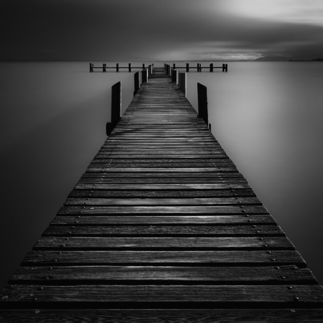 A wooden pier in Lac Léman (Lake Geneva) at Préverènges beach during sunset, in black & white. Shadows & Light - Copyright Johan Peijnenburg - NiO Photography