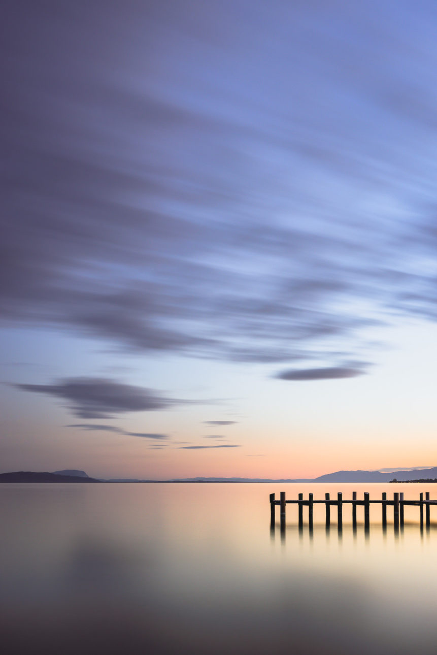 A lake landscape featuring a colourful sunset at Lac Léman (Lake Geneva), with a wooden pier, near Préverenges in Switzerland. Colourful tranquillity at Lac Léman - Copyright Johan Peijnenburg - NiO Photography