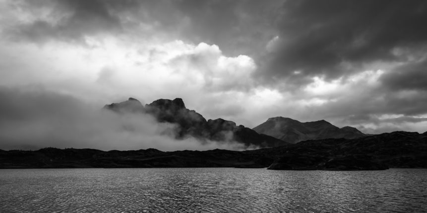 A moody mountain lake sunset at Laghetto Moesola, a small Swiss lake situated at the summit of the San Bernardino Pass. In the background the mountains Piz Uccello and Piz de la Lumbreida. Mountain Moods - Copyright Johan Peijnenburg - NiO Photography