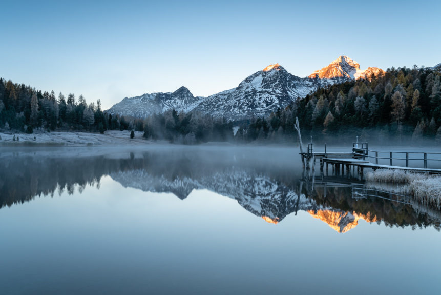 A Swiss mountain lake landscape, featuring a sunrise with alpenglow, a pier and mountain reflections at Lej da Staz (Stazersee) in St. Moritz. A Chilly Rise - Copyright Johan Peijnenburg - NiO Photography