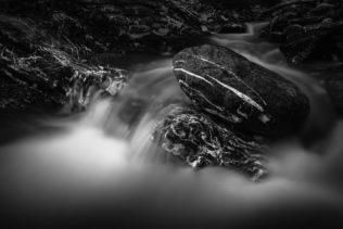 A fine art long exposure of an alpine mountain river rapid in black & white, featuring white water and dark marbled rocks with white streaks. Marbled - Copyright Johan Peijnenburg - NiO Photography