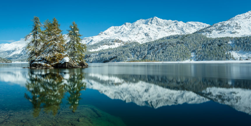 A lake landscape, featuring larch trees with fall colours and the reflection of Piz Corvatsch mountain with autumn snow at Lake Sils (Silsersee). Autumn Snow - Copyright Johan Peijnenburg - NiO Photography