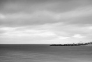 An expansive mountaintop view of the Norwegian Sea near Lofoten with a lighthouse, a coastal islands, and the mountains of Lofoten, Norway. A Norse View - Copyright Johan Peijnenburg - NiO Photography