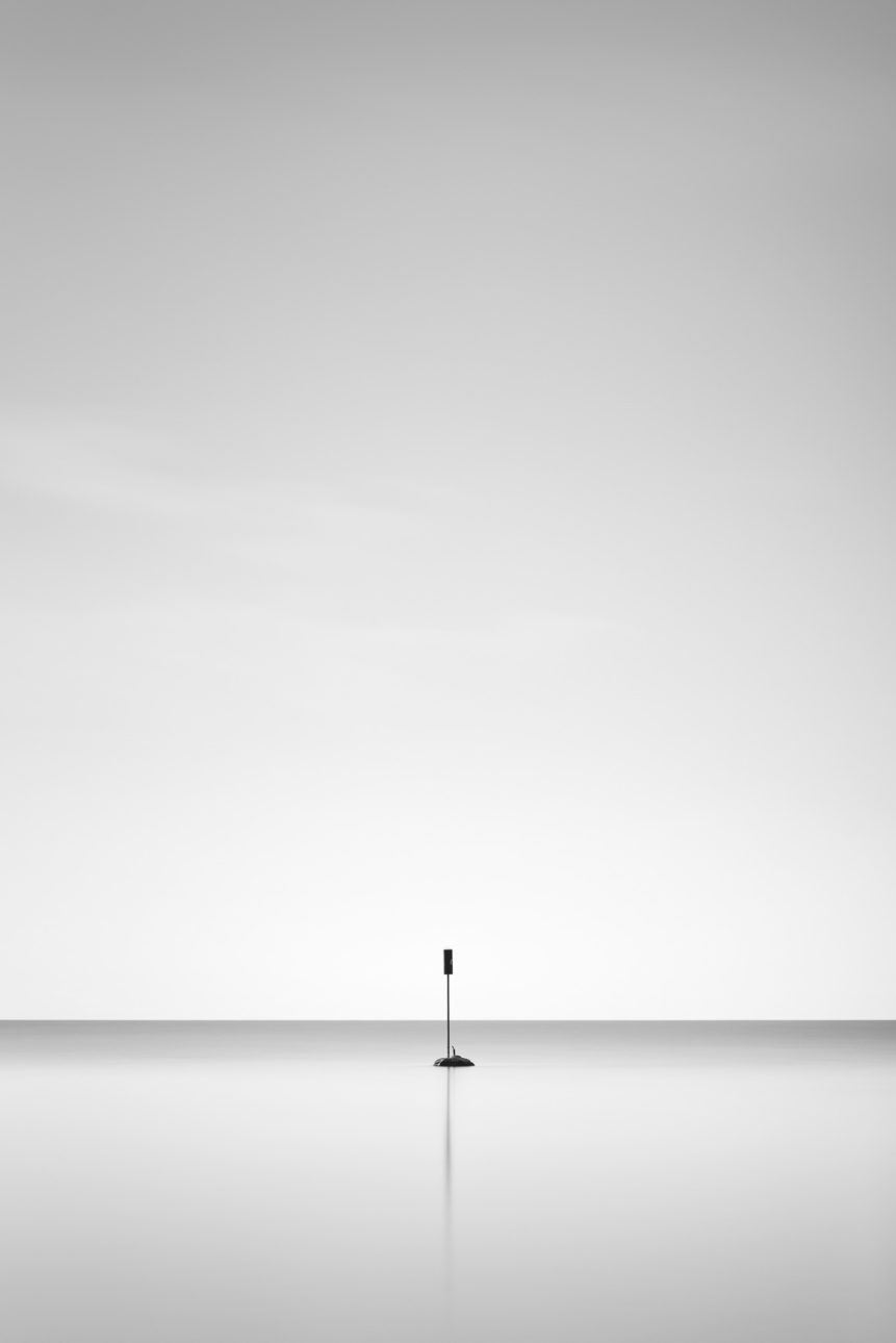 A minimalist landscape in black & white, featuring a solitary signpost and its reflection in Lac Léman (Lake Geneva). One - Copyright Johan Peijnenburg - NiO Photography