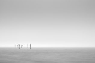 A minimalist Dutch coastal landscape in B&W with signposts at the coast of the Oosterschelde near Tholen in Zeeland on a foggy day. Passage - Copyright Johan Peijnenburg - NiO Photography