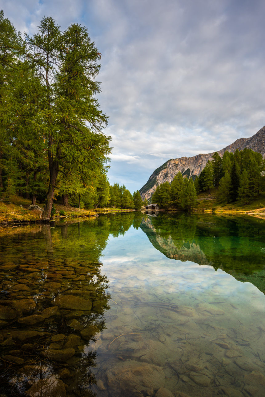 A mountain lake landscape, showing a quiet sunrise at Lai da Palpuogna in autumn with larch trees and mountains reflected in the lake. Dawning - Copyright Johan Peijnenburg - NiO Photography