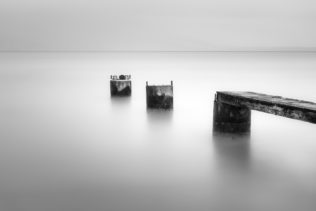 A minimalist misty lake landscape in black & white, showing the remains of an abandoned pier in Lac de Neuchâtel in Switzerland. Broken - Copyright Johan Peijnenburg - NiO Photography