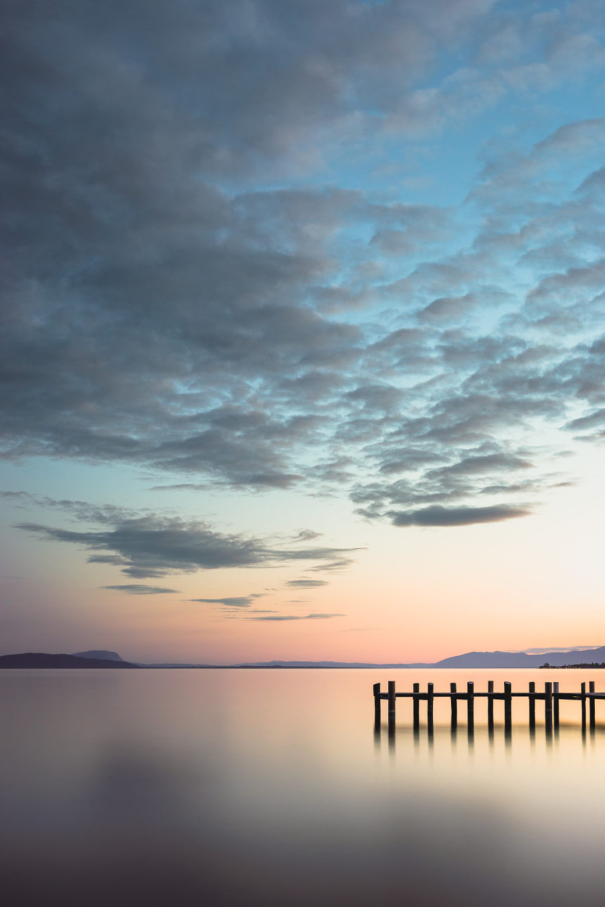 A colourful sunset with gorgeous clouds at Lac Léman (Lake Geneva), with a small wooden pier in the foreground. At the beach - Copyright Johan Peijnenburg - NiO Photography