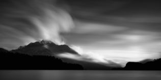 A minimalist lake landscape in B&W, showing an eruption of clouds above the Piz de La Margna and the Swiss Alps at Lake Sils in Engadin. Eruption - Copyright Johan Peijnenburg - NiO Photography