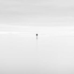 A minimalist photograph in black & white with a dreamy and soothing look and feel, featuring a signpost in Lac de Neuchâtel on a foggy and hazy day. Yield - Copyright Johan Peijnenburg - NiO Photography