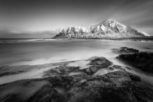 A coastal mountain landscape in B&W, showing a Skagsanden beach with Hustinden mountain in Lofoten, Norway, in winter. Nordic Sunrise - Copyright Johan Peijnenburg - NiO Photography