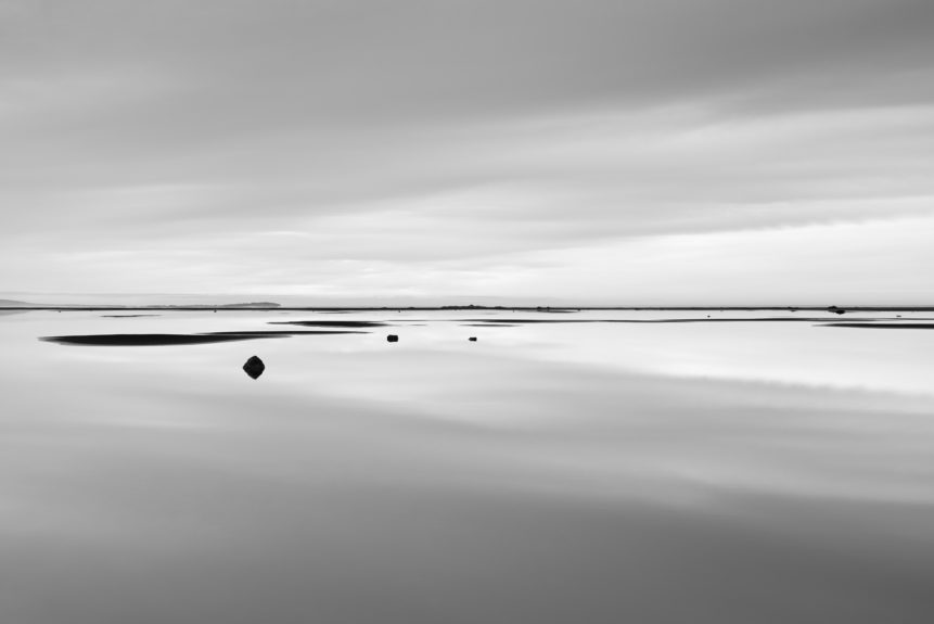 A minimalist Icelandic coastal landscape in B&W with cloud reflections on a lagoon with rocks near Stokksnes beach. Still Waters - Copyright Johan Peijnenburg - NiO Photography