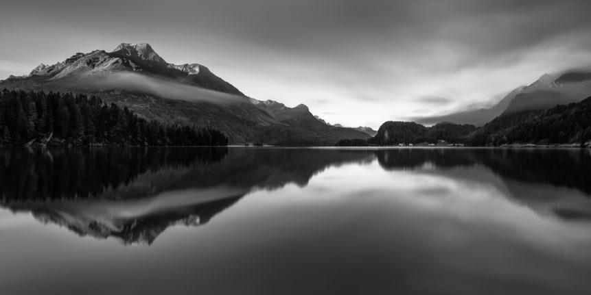 A lake landscape in black & white, featuring the mountain reflections of the Alps at sunrise in a quiet lake near Sils im Engadin, Switzerland. The main mountain in the back is Piz de la Margna. Alpine Stillness - Copyright Johan Peijnenburg - NiO Photography