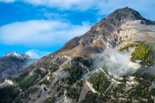 A mountain landscape, featuring the Alps in fall with larch trees in their fall colours and a bit of rising fog bathing in early morning light. This mountain landscape was captrured near Zernez in the Swiss National Park. Carved - Copyright Johan Peijnenburg - NiO Photography