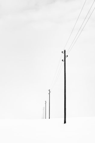 A winter landscape photograph in B&W, with telephony poles disappearing towards the horizon in a foggy and snowy Swiss winter landscape. Fading - Copyright Johan Peijnenburg - NiO Photography