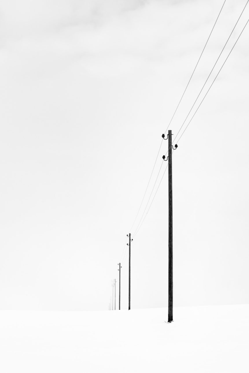 A winter landscape photograph in B&W, with telephony poles disappearing towards the horizon in a foggy and snowy Swiss winter landscape. Fading - Copyright Johan Peijnenburg - NiO Photography