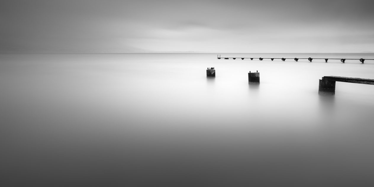 A soothing minimalist lake landscape in black & white,  with two abandoned piers in a tranquil lake ( Lac de Neuchâtel) on a foggy day. Tranquillity - Copyright Johan Peijnenburg - NiO Photography