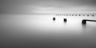 A soothing minimalist lake landscape in black & white,  with two abandoned piers in a tranquil lake ( Lac de Neuchâtel) on a foggy day. Tranquillity - Copyright Johan Peijnenburg - NiO Photography