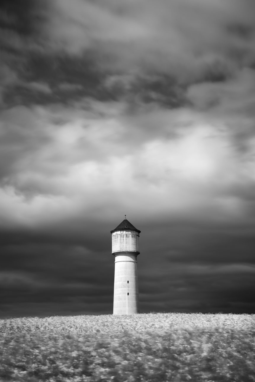 A landscape in B&W, showing a white water tower in a rapeseed flower field just before the storm in the Swiss countryside. Fearless - Copyright Johan Peijnenburg - NiO Photography