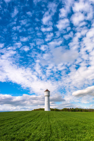 The Swiss countryside in spring, featuring a white water tower in a green field against a big blue sky with puffy clouds. Refreshing - Copyright Johan Peijnenburg - NiO Photography