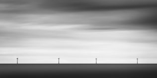 A minimalist coastal landscape in B&W, featuring four windmills (turbines) at work in the Irish Sea near Arklow in County Wicklow, Ireland. Teamwork - Copyright Johan Peijnenburg - NiO Photography