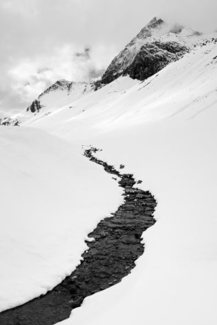 A landscape in B&W of winter in the Alps, featuring a mountain river finding its way down from the Swiss Alps near the Albula pass. Cold River - Copyright Johan Peijnenburg - NiO Photography